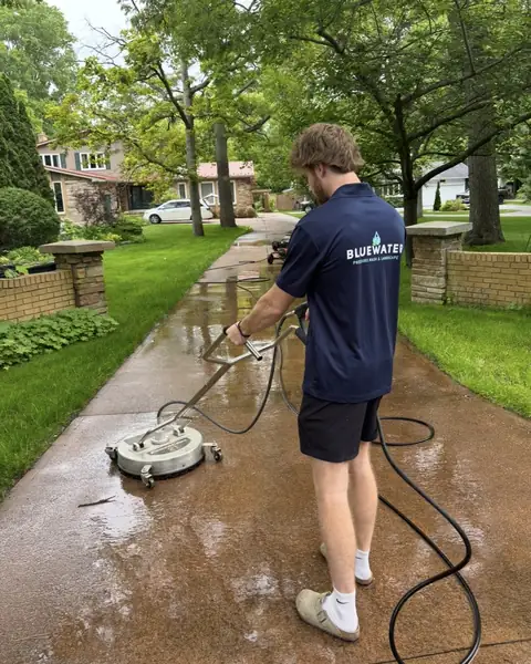 Mitch Guerette in a Bluewater shirt running a surface cleaner on a concrete driveway
