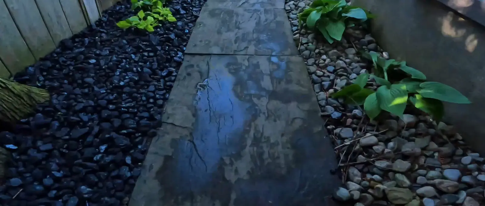 Stone walkway between beds of black river rock and hostas beside a house, Sarnia-area landscaping