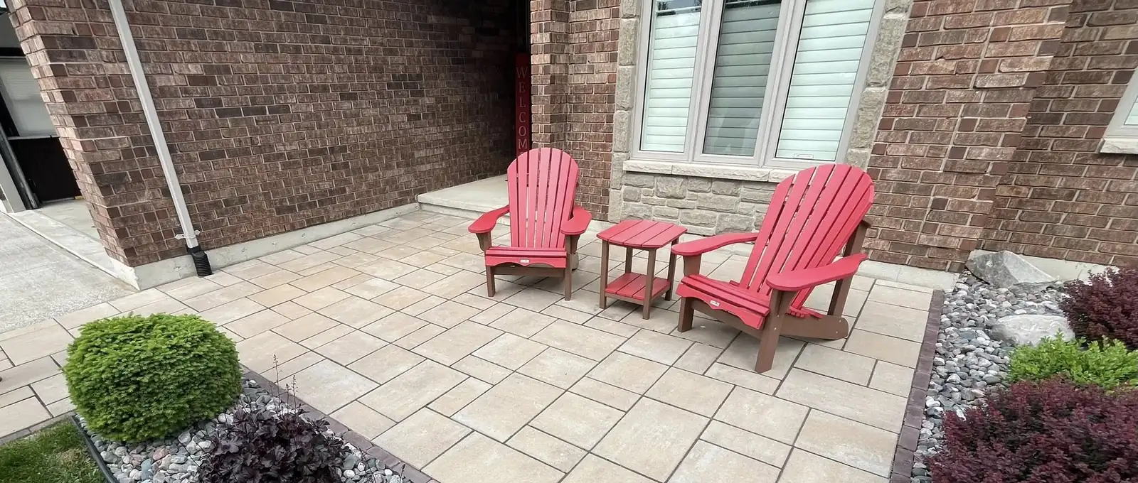 Front-entry paver patio with red Adirondack chairs and a stone border in Sarnia, Ontario