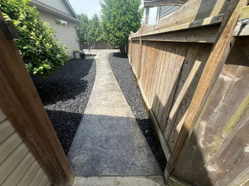 Side yard with a concrete walkway and beds of dark stone