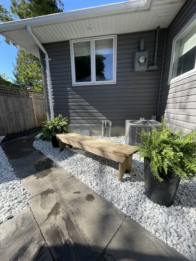 White stone bed with a cedar bench and ferns beside a home